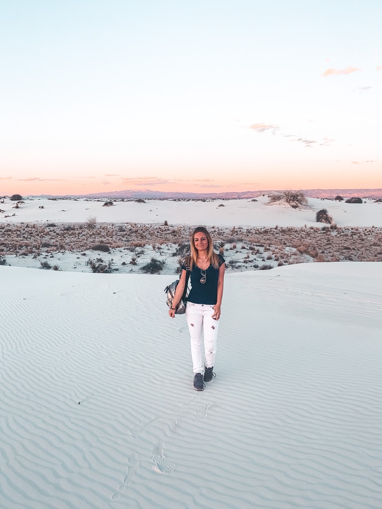 The author stands on the smooth, undulating dunes of White Sands, the sunset casting a soft glow on the landscape and her casual, exploratory stance.