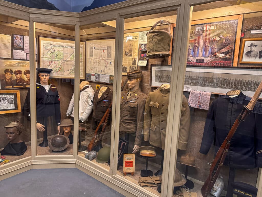 Military memorabilia display at the Tularosa Basin Museum of History, including uniforms, helmets, and rifles from different eras