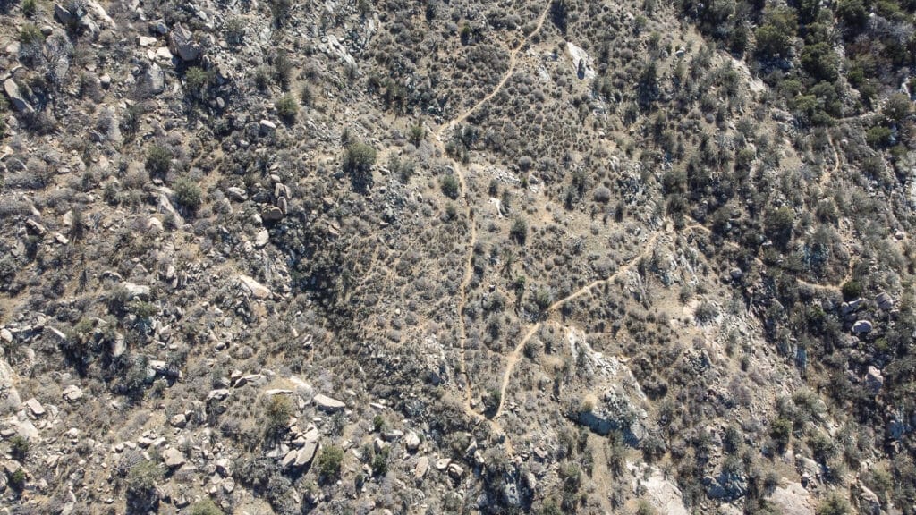 Close aerial snapshot of the pine tree loop trail snaking through a rocky terrain with sparse vegetation. The shadows indicate a sunny day, and the path looks well-trodden, inviting hikers to explore.
